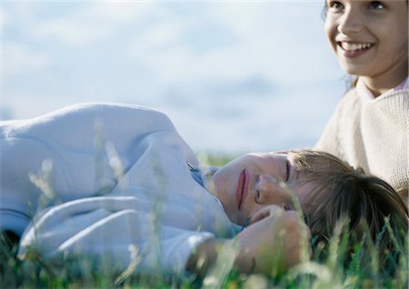 Boy lying on grass with eyes closed, girl behind him Stock Photo - Premium Royalty-Free, Code: 695-05777410