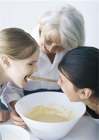 Grandmother baking with granddaughters, one girl tasting batter Stock Photo - Premium Royalty-Free, Code: 695-05777525