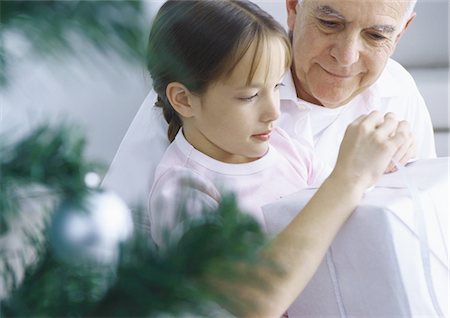 Girl and grandfather opening package, Christmas tree branches in foreground Stock Photo - Premium Royalty-Free, Code: 695-05777529