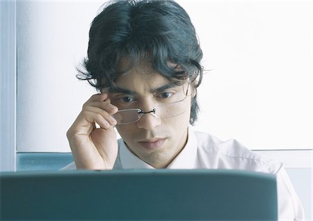 Businessman looking down at computer screen, looking over glasses Foto de stock - Sin royalties Premium, Código: 695-05777568