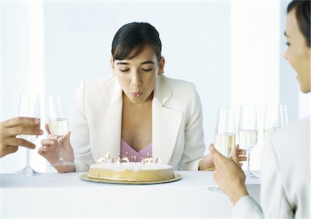 Woman blowing out candles on cake, sitting with other people, holding glasses of champagne Stock Photo - Premium Royalty-Free, Code: 695-05777609