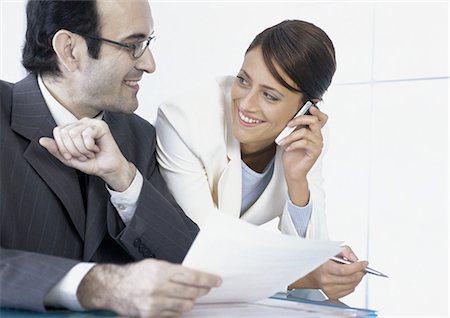 simsearch:695-05776257,k - Businesswoman talking on cell phone smiling at businessman next to her Stock Photo - Premium Royalty-Free, Code: 695-05777600