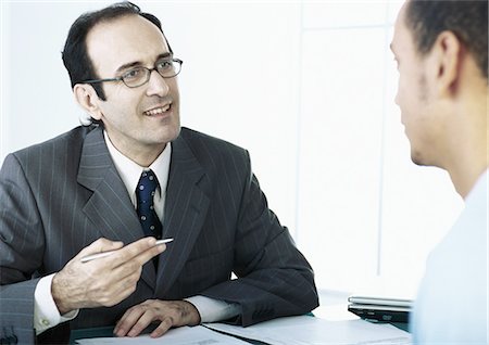 Businessman gesturing with pen in hand, speaking to man Stock Photo - Premium Royalty-Free, Code: 695-05777602