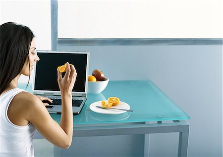 Woman sitting at table with laptop, eating fruit Stock Photo - Premium Royalty-Free, Code: 695-05777733