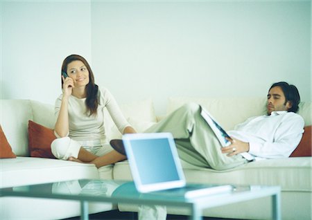 Young couple sitting on couch, man reading while woman uses cell phone Stock Photo - Premium Royalty-Free, Code: 695-05778229