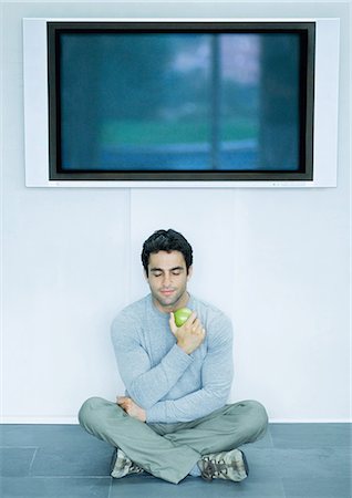 eating and tv - Man sitting on floor, eating apple, widescreen TV on wall over head Stock Photo - Premium Royalty-Free, Code: 695-05779068