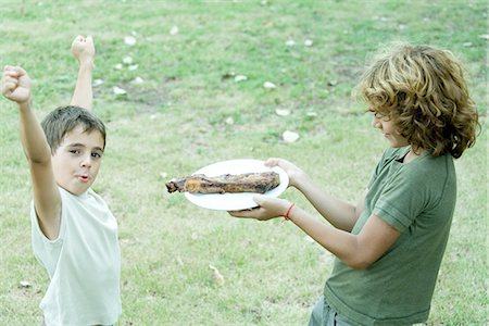 Boy handing friend plate of grilled meat Stock Photo - Premium Royalty-Free, Code: 695-05779120