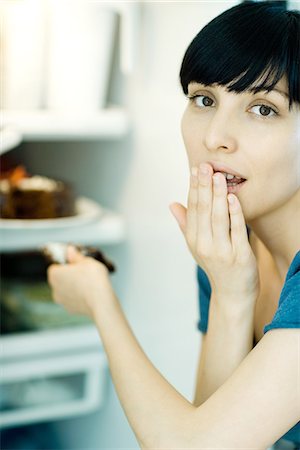 simsearch:695-05779160,k - Young woman taking slice of cake from refrigerator, looking at camera, covering mouth Stock Photo - Premium Royalty-Free, Code: 695-05779159