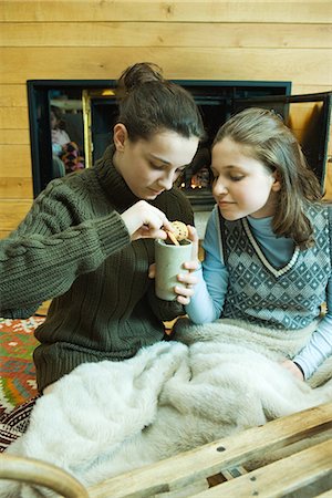 Two teenage girls sitting by fireplace, sharing snack Stock Photo - Premium Royalty-Free, Code: 695-05779175