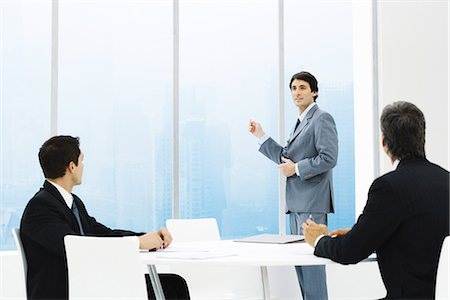 Businessmen in meeting, one standing, pointing out window Stock Photo - Premium Royalty-Free, Code: 695-05779283