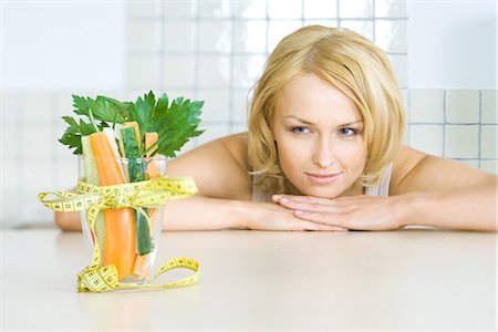 Young woman looking at glass of fresh vegetables with a measuring tape bow Stock Photo - Premium Royalty-Free, Code: 695-05779317