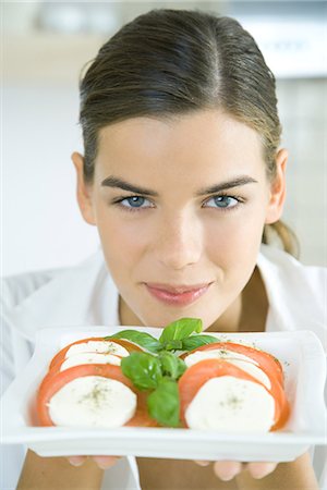 Jeune femme brandissant une assiette de salade de tomates mozzarella, souriant à la caméra Photographie de stock - Premium Libres de Droits, Code: 695-05779319