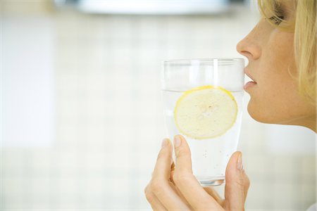 sparkling water closeup - Woman holding a glass of water with a slice of lemon up to her lips, profile Stock Photo - Premium Royalty-Free, Code: 695-05779325