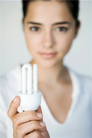 fluorescent light bulb - Young woman holding energy efficient light bulb, focus on foreground Stock Photo - Premium Royalty-Free, Code: 695-05779394