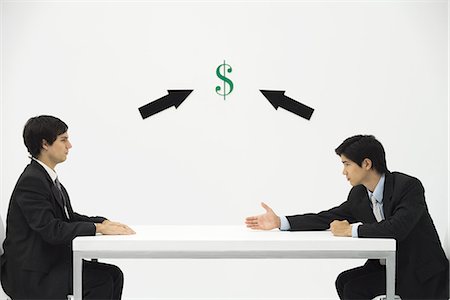 Two businessmen face to face, one reaching to offer his hand, dollar sign and arrows between them Stock Photo - Premium Royalty-Free, Code: 695-05779426