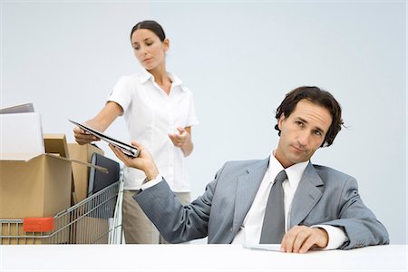 silhouette of businessman standing in office - Man handing binder back to assistant, shopping cart full of boxes nearby Stock Photo - Premium Royalty-Free, Code: 695-05779468