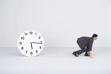 running start - Businessman crouching, ready to run, next to clock Stock Photo - Premium Royalty-Free, Code: 695-05779566