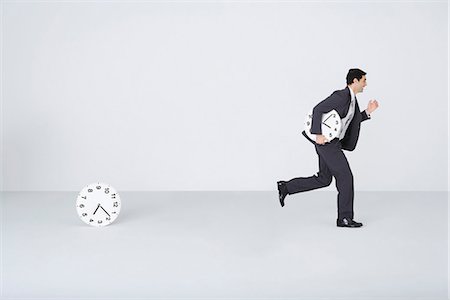 Businessman running with clock, leaving second clock behind Fotografie stock - Premium Royalty-Free, Codice: 695-05779561