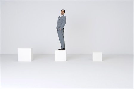 progression concept - Businessman standing on block with hands in pockets, smiling at camera Stock Photo - Premium Royalty-Free, Code: 695-05779563