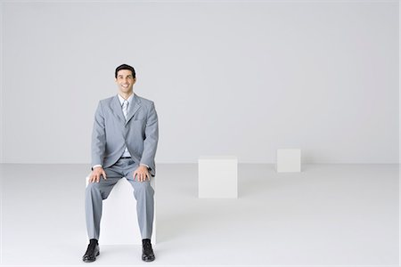 pedestal - Businessman sitting on block, smiling at camera Stock Photo - Premium Royalty-Free, Code: 695-05779572