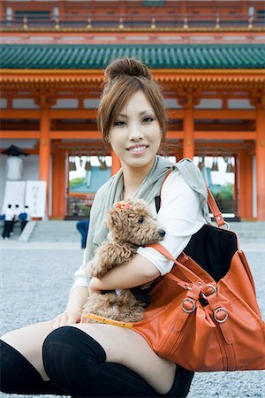 fashion woman dog - Young female crouching in front of pagoda, holding small dog, portrait Stock Photo - Premium Royalty-Free, Code: 695-05779615