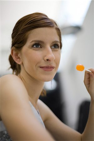 Young woman holding lollipop, looking away Stock Photo - Premium Royalty-Free, Code: 695-05779651