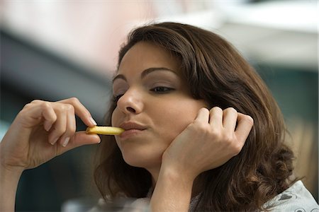 spuntino - Young woman eating french fries, hand under chin Fotografie stock - Premium Royalty-Free, Codice: 695-05779679