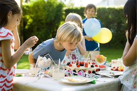 Garçon de souffler les bougies sur le gâteau d'anniversaire à la fête d'anniversaire en plein air Photographie de stock - Premium Libres de Droits, Code: 695-05779975