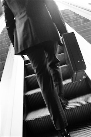 Businessman carrying briefcase ascending escalator, rear view Foto de stock - Sin royalties Premium, Código: 695-05770029