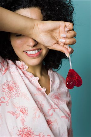 embarrassed female - Woman smiling, covering eyes with arm, holding heart-shaped lollipop Stock Photo - Premium Royalty-Free, Code: 695-05770304
