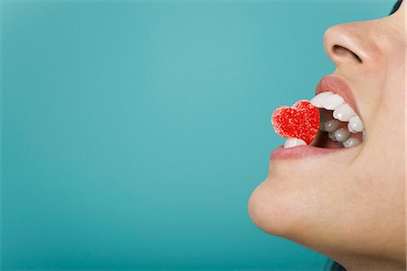 Woman holding heart-shaped candy between teeth, cropped Stock Photo - Premium Royalty-Free, Code: 695-05770306