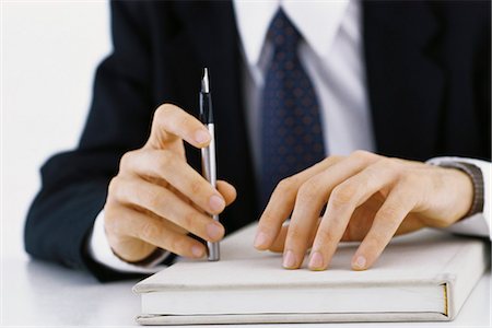 Businessman's hands on book, holding pen, cropped view Stock Photo - Premium Royalty-Free, Code: 695-05770429