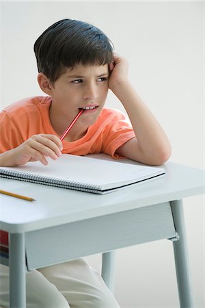 Elementary school student sitting at desk, leaning on elbow, chewing end of pencil Foto de stock - Royalty Free Premium, Número: 695-05770508