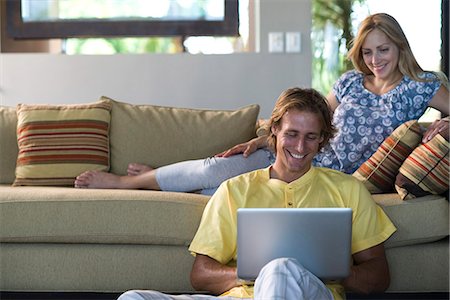 Couple together in living room, woman reclining on sofa, man sitting on floor with laptop computer Stock Photo - Premium Royalty-Free, Code: 695-05770744