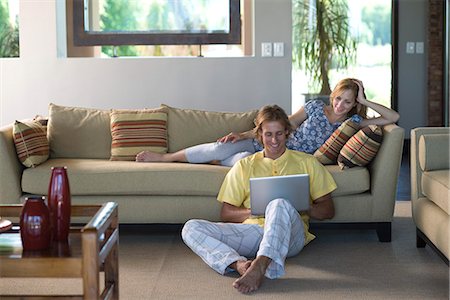 Couple together in living room, woman reclining on sofa, man sitting on floor with laptop computer Stock Photo - Premium Royalty-Free, Code: 695-05770743