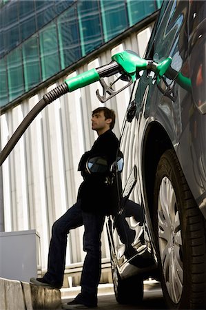 Man at gas station leaning against car waiting to finish refueling Stock Photo - Premium Royalty-Free, Code: 695-05771032