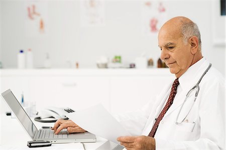 simsearch:695-05771285,k - Doctor at desk busy with paperwork Foto de stock - Royalty Free Premium, Número: 695-05771279