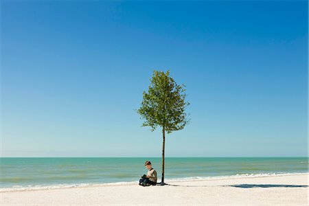 simsearch:632-05553524,k - Boy reading book under tree growing on beach Stock Photo - Premium Royalty-Free, Code: 695-05771510