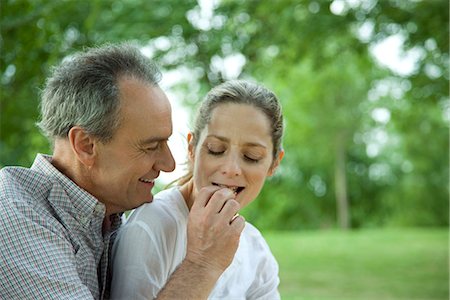 photo of a woman feeding her husband food - Mature couple together in park, man feeding woman Stock Photo - Premium Royalty-Free, Code: 695-05771584