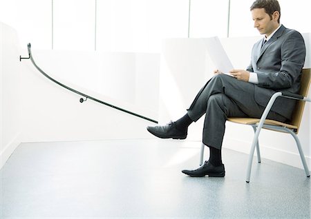 Businessman sitting on chair with legs crossed, looking at document Stock Photo - Premium Royalty-Free, Code: 695-05771965