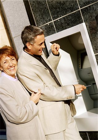 Man and woman in jackets at ATM machine, smiling Stock Photo - Premium Royalty-Free, Code: 695-05773214