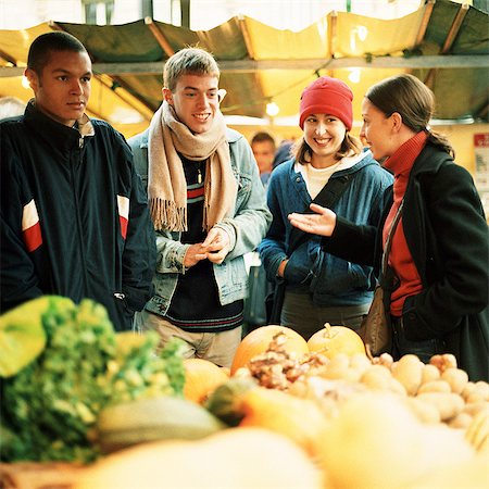 Young people at produce market, fruits and vegetables blurred in foreground Stock Photo - Premium Royalty-Free, Code: 695-05773223