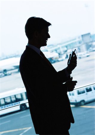people airports silhouettes - Businessman looking at cellular phone in airport, silhouette. Stock Photo - Premium Royalty-Free, Code: 695-05773247