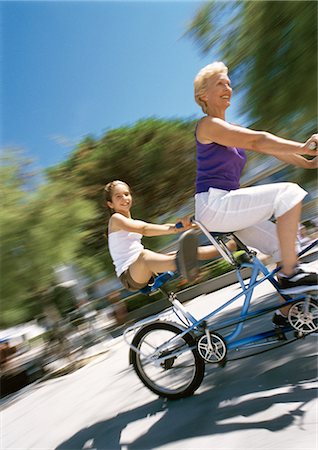 Mature woman and girl riding tandem bike, granddaugher sticking her legs out, blurred Stock Photo - Premium Royalty-Free, Code: 695-05773393