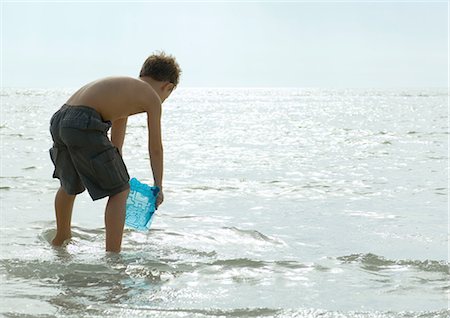 rear view of a boy bending over - Boy filling bucket with water in surf Stock Photo - Premium Royalty-Free, Code: 695-03374044