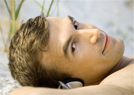 Man lying on sand, listening to headphones Stock Photo - Premium Royalty-Free, Code: 695-03374100