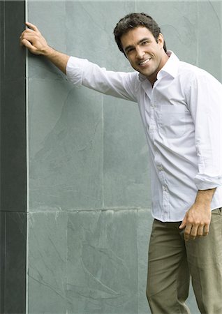 Man standing with hand on wall, smiling at camera, portrait Stock Photo - Premium Royalty-Free, Code: 695-03374308
