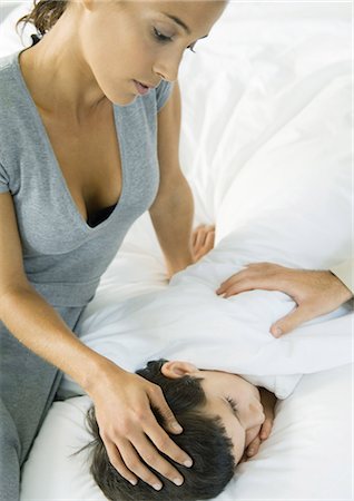 side view woman laying down head - Child lying in bed, mother's hand on head and father's hand on shoulder Stock Photo - Premium Royalty-Free, Code: 695-03374393