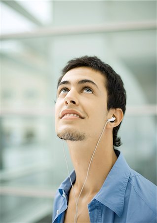 Young man listening to earphones, looking up Stock Photo - Premium Royalty-Free, Code: 695-03374448