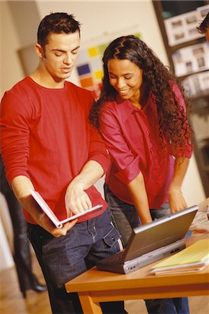 Young man and woman standing next to laptop, man pointing to user's manual Stock Photo - Premium Royalty-Free, Code: 695-03374569